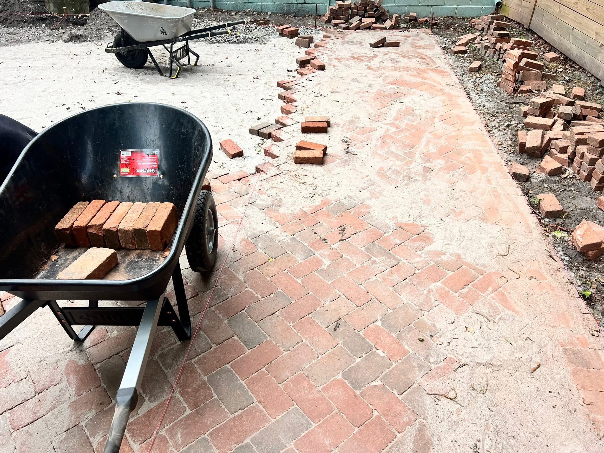 Reclaimed brick being laid in herringbone on a screeded sand bed with string lines