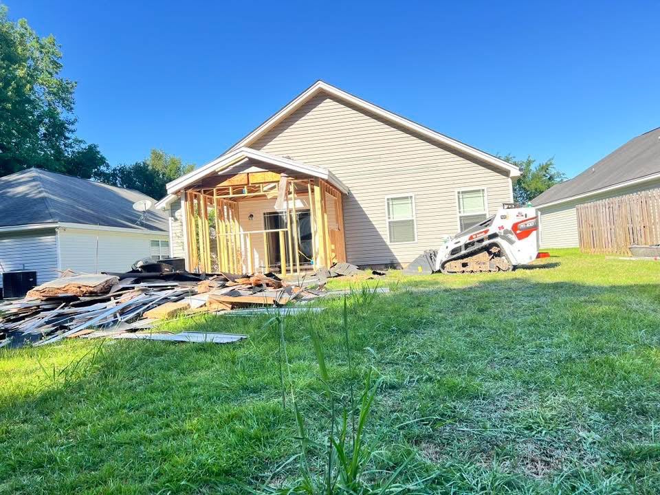 Old porch torn off a house with debris stacked and a skid steer on site