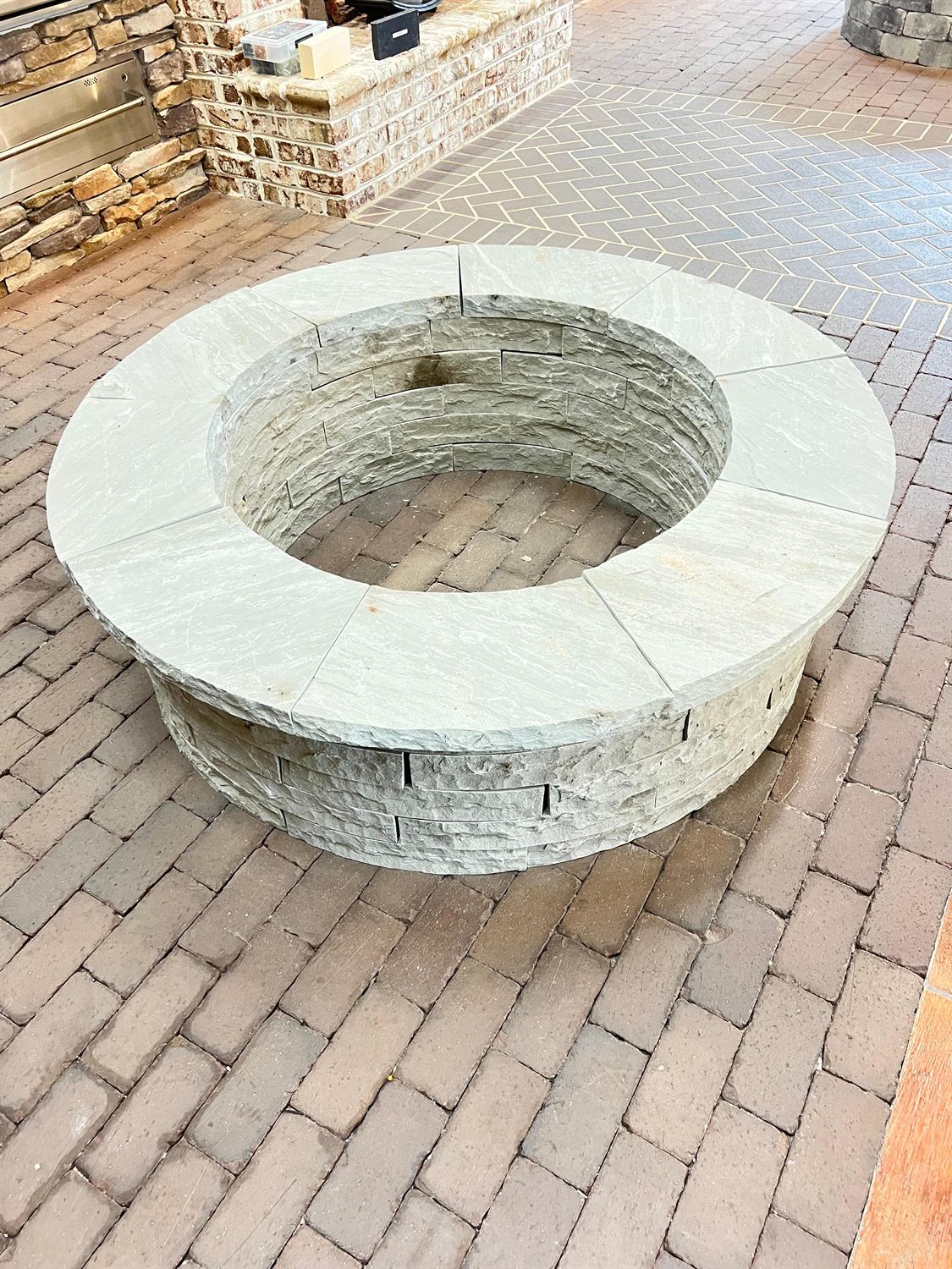 Round fire pit in stone veneer with a wide flagstone cap, built by Lalo's Home Improvements