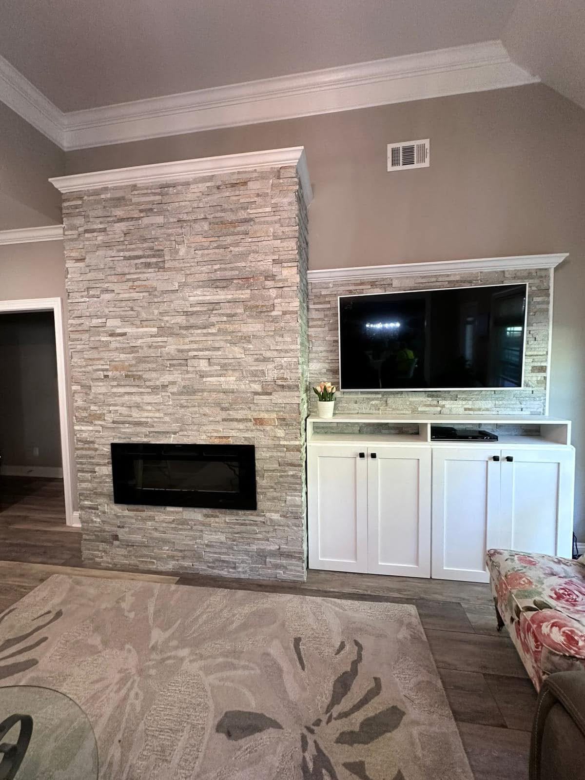 Living room with a stacked stone fireplace wall, mounted TV and white built-in cabinets