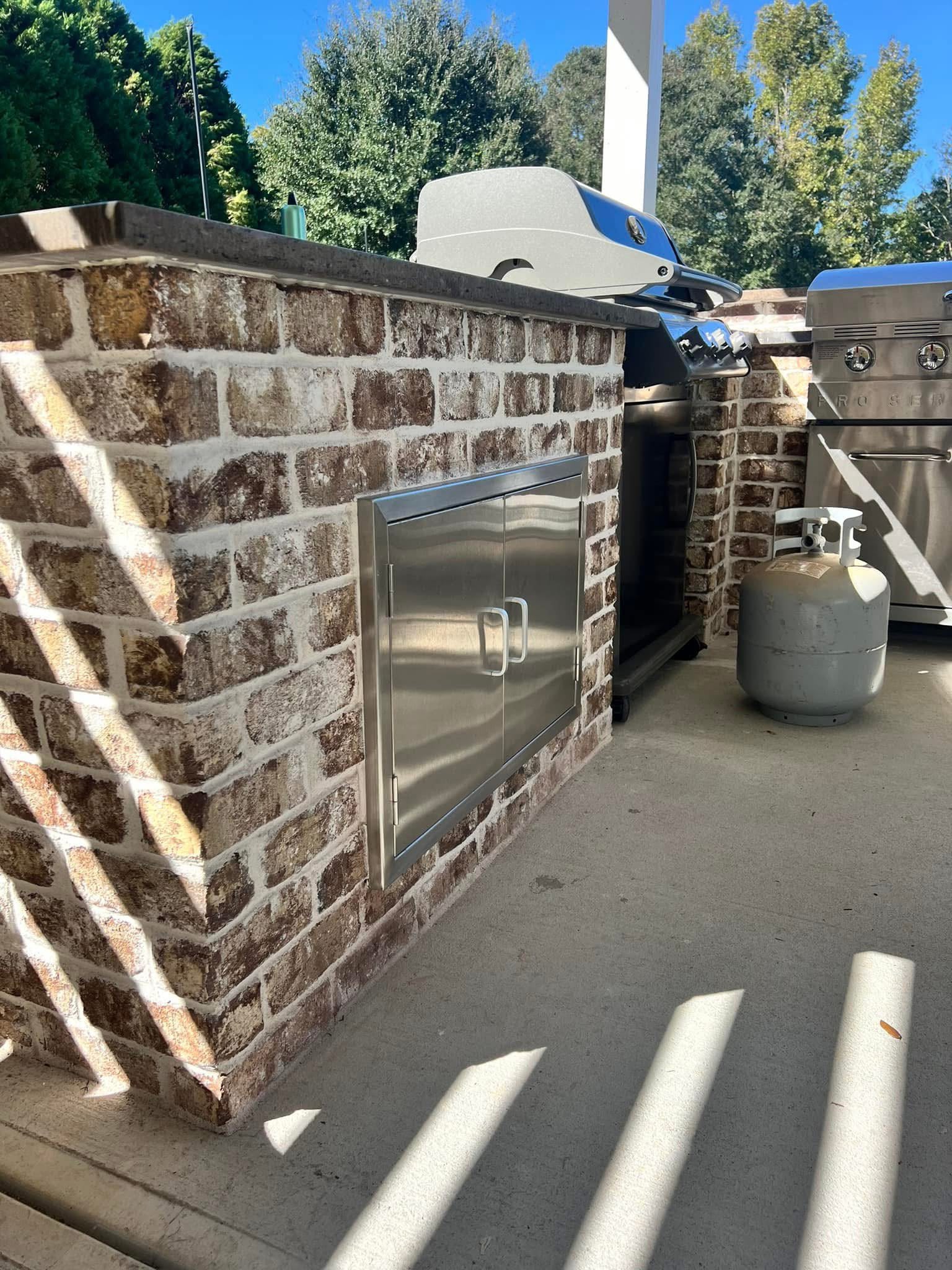 Brick outdoor kitchen counter with stainless access doors and a built-in grill