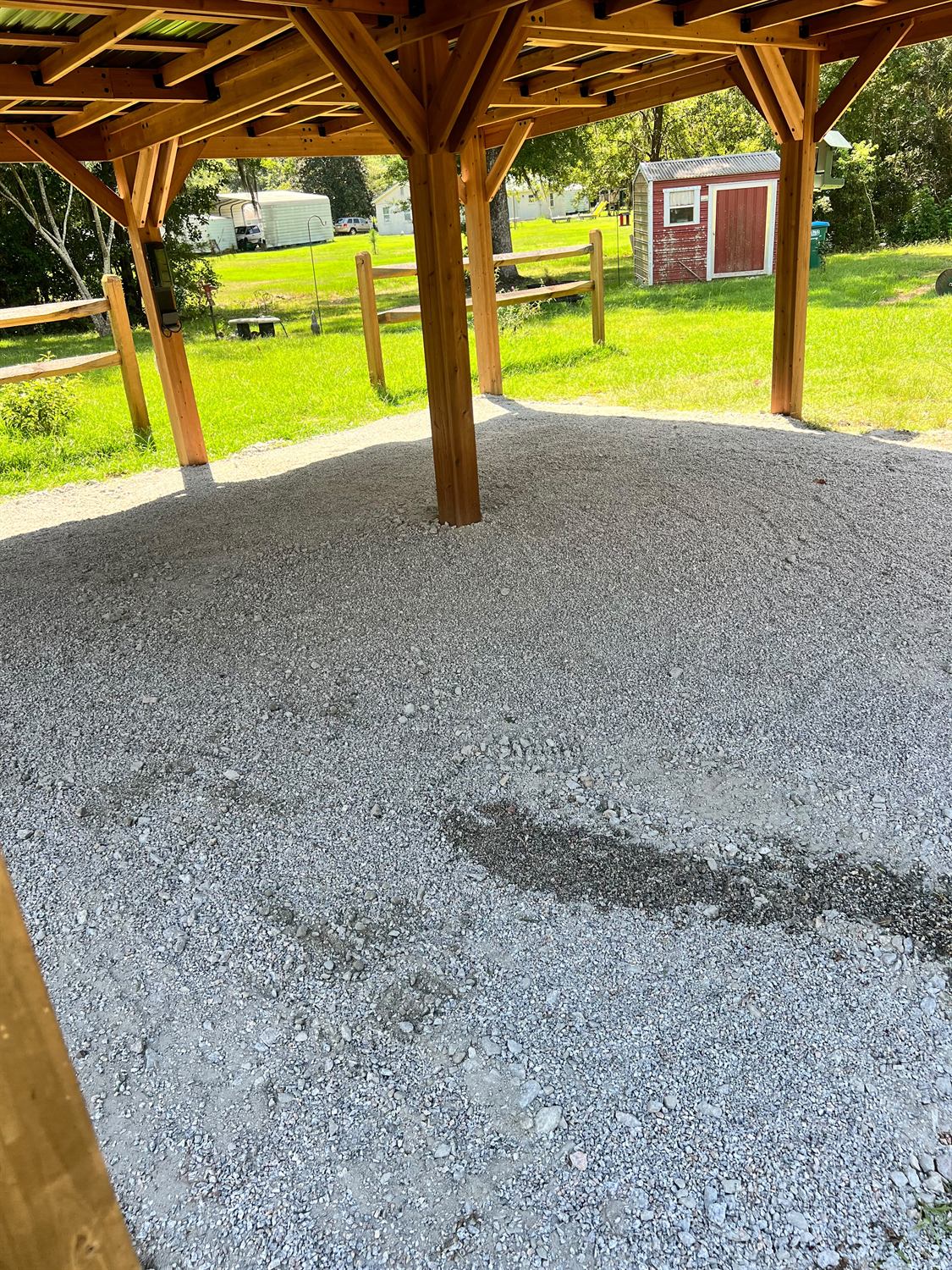 Underside of the cedar pavilion showing the rafters and the compacted gravel floor