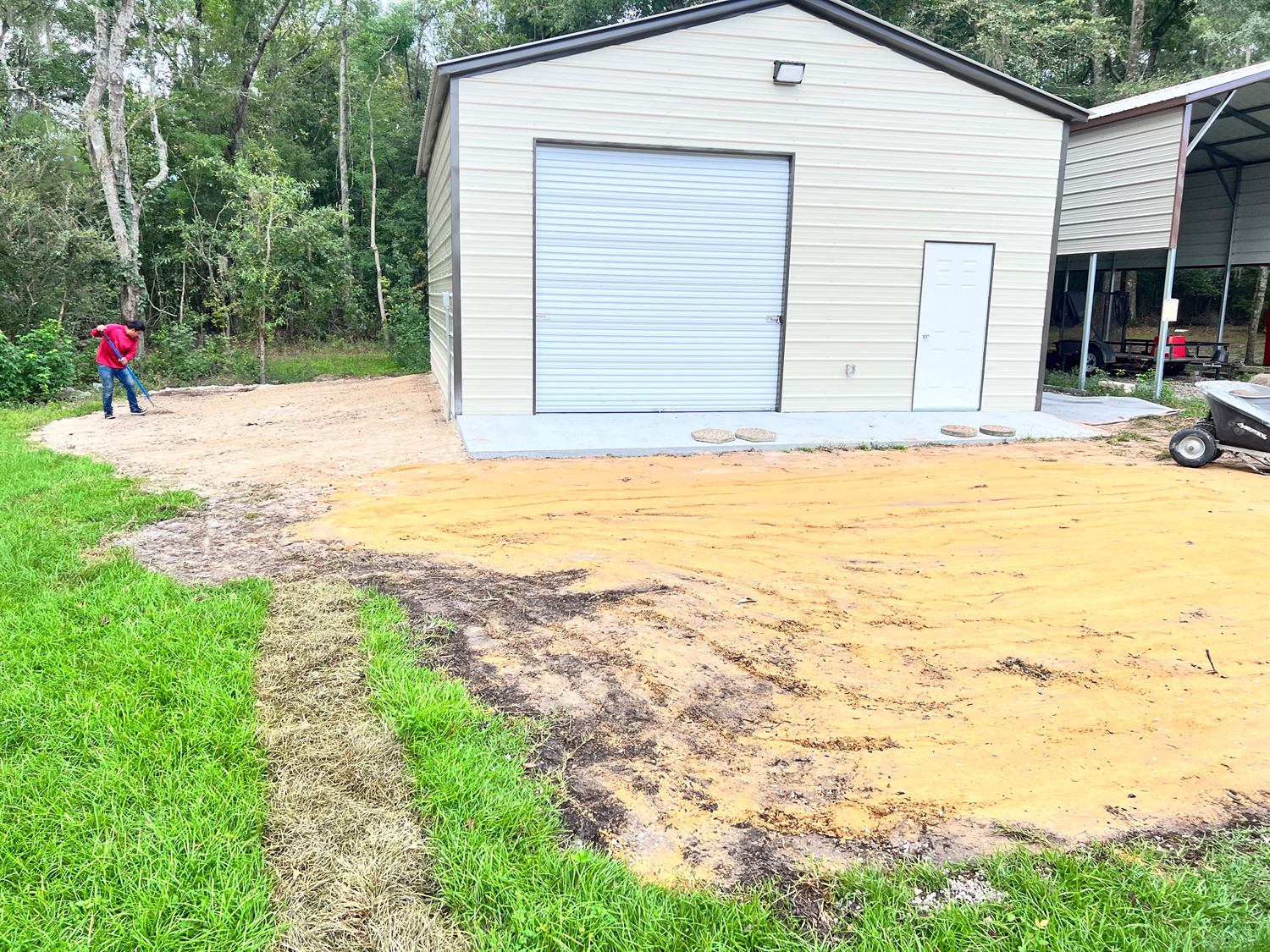 Graded sand pad beside a metal building being raked level before sod goes down