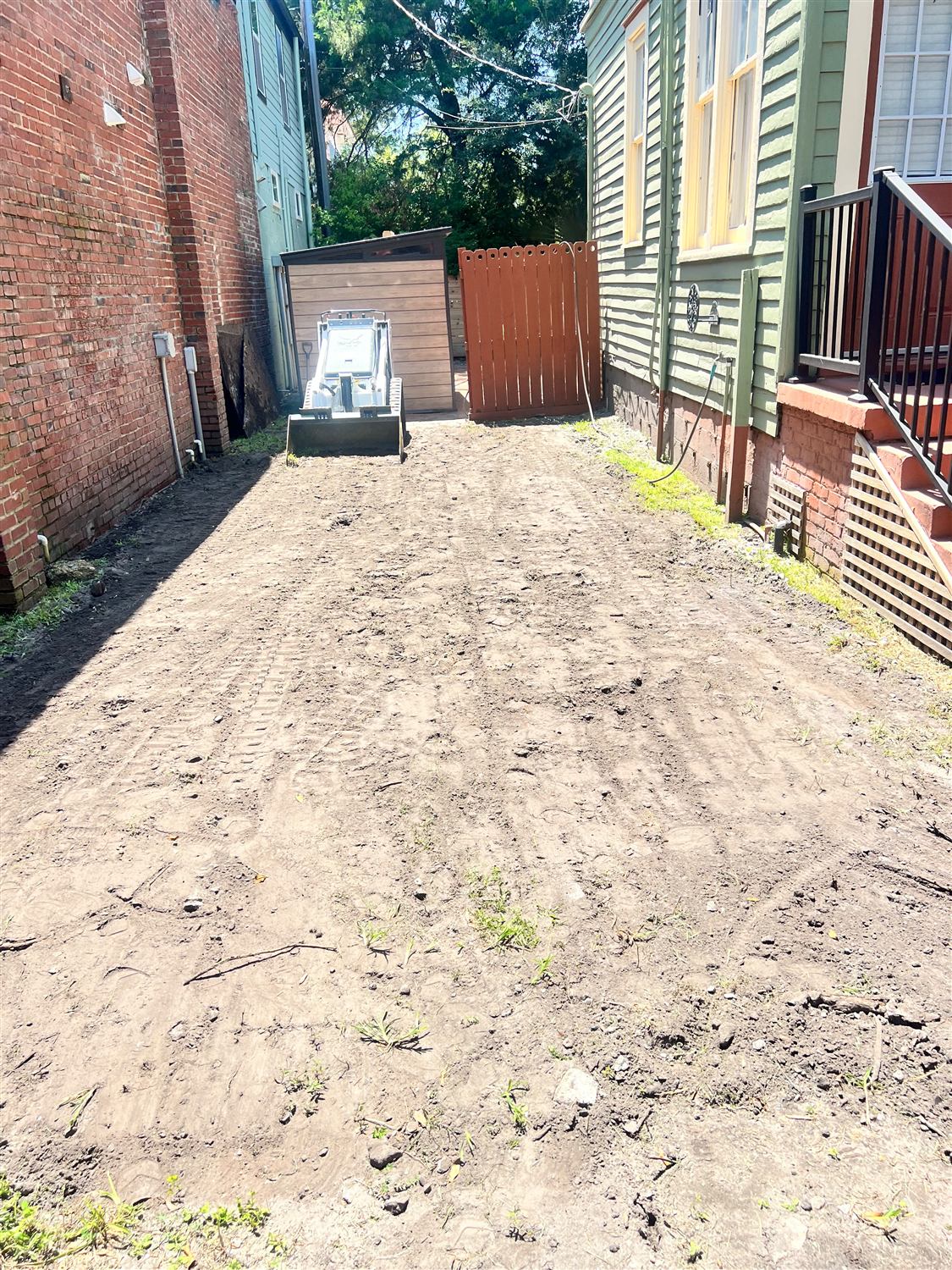 Narrow side yard graded flat with a compact track loader on site