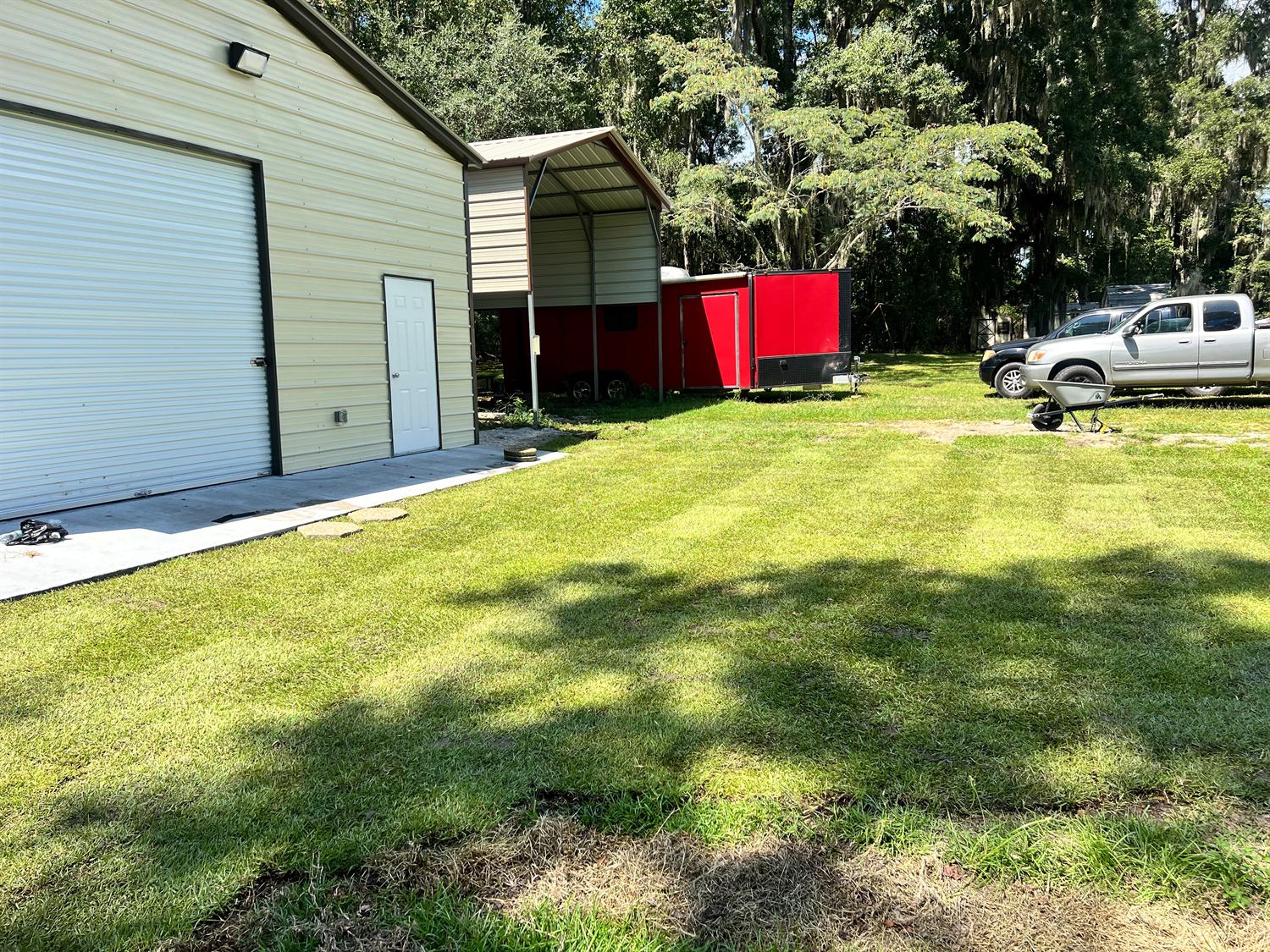 New sod lawn beside a metal garage with a trailer parked under the awning