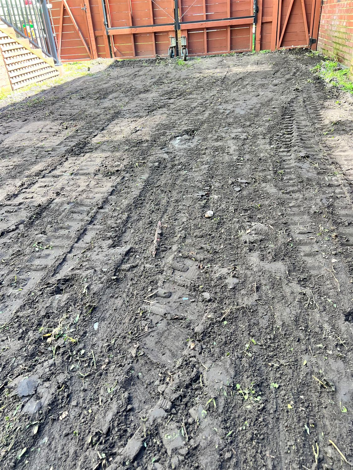 Side yard stripped and graded in front of a wood gate, before gravel